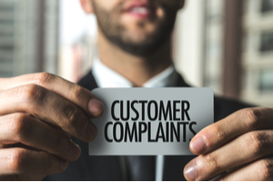 a man in black suit is holding a paper card that says customer complaints