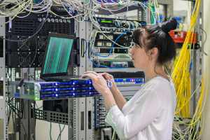A woman with a laptop in a server room.