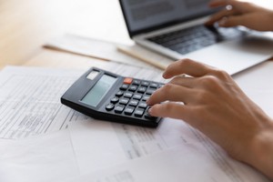 Person calculating cost of software development services in calculator and laptop