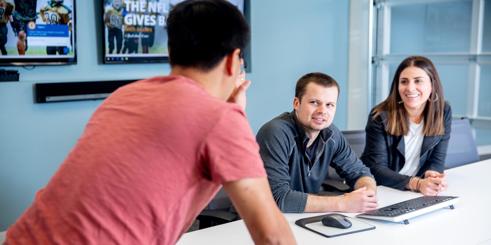 man in red tshirt talking to teammates during a meeting