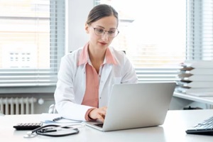 doctor looking at medical billing and coding software on computer sitting on desk