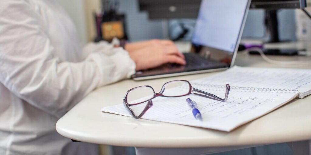 women working on laptop while putting specs and pen on the table