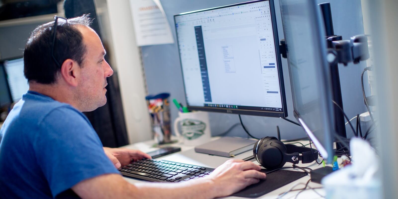 man working at a desk with dual monitors, focusing on an ai data processing spreadsheet or document on the screen